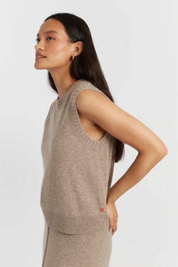 Woman wearing a beige sleeveless sweater against a white background