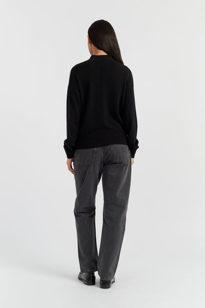 Person wearing a black sweater and gray pants on a white background