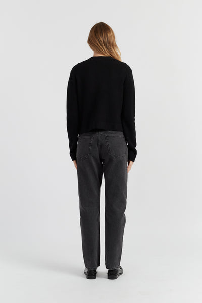 Person wearing a black sweater and gray pants on a white background