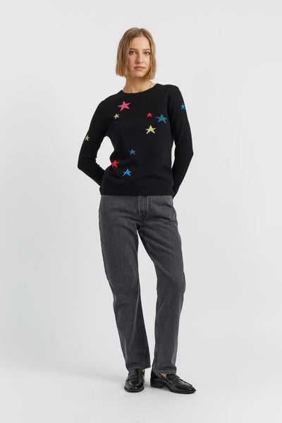 Person wearing a black sweater with colorful star patterns and gray pants on a white background
