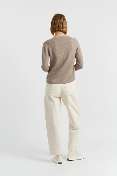 Person wearing a brown sweater and white pants on a white background