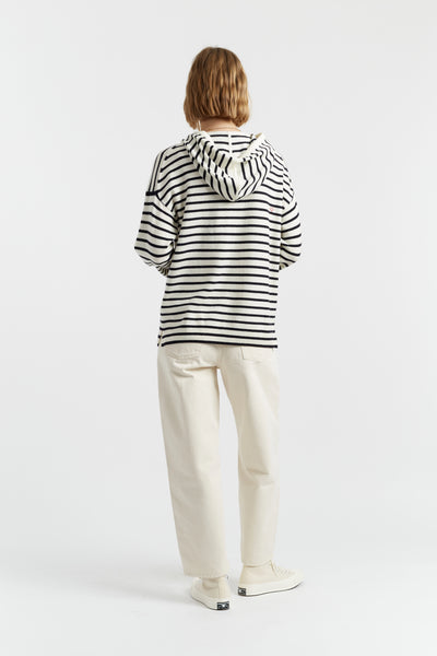 Person wearing a black and white striped hoodie and beige pants on a white background