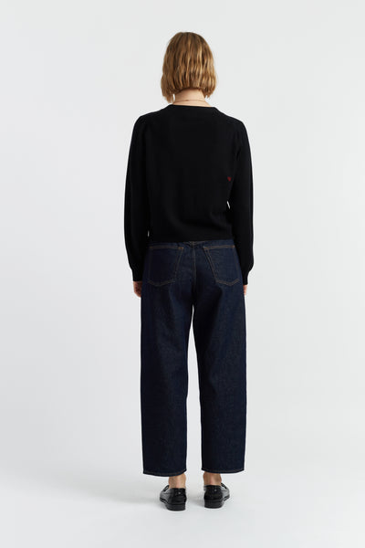 Person wearing a black sweater and dark jeans on a white background