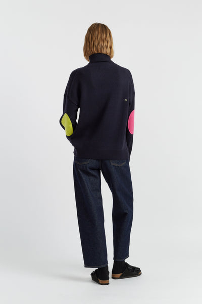 Person wearing a navy sweater with colorful sleeves on a white background