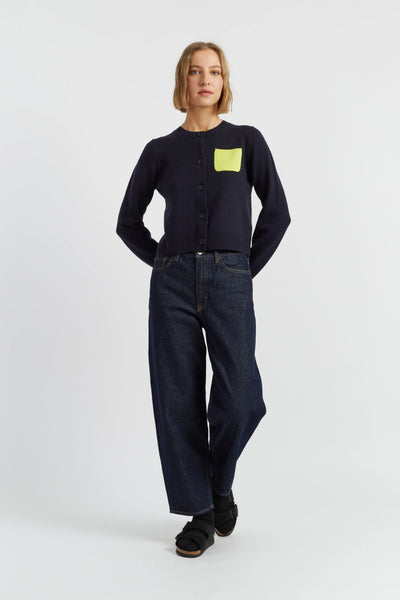 Person wearing a black sweater with a yellow pocket and dark jeans on a white background