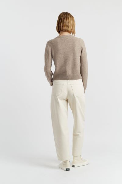 Person wearing a beige sweater and white pants on a white background