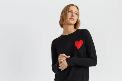 Woman wearing a black sweater with a red heart on a light gray background