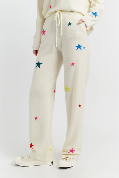 Cream-colored sweatpants with colorful star patterns worn by a person on a white background