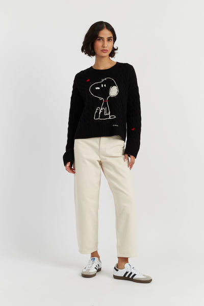 Person wearing a black sweater with a dog design and white pants on a light gray background