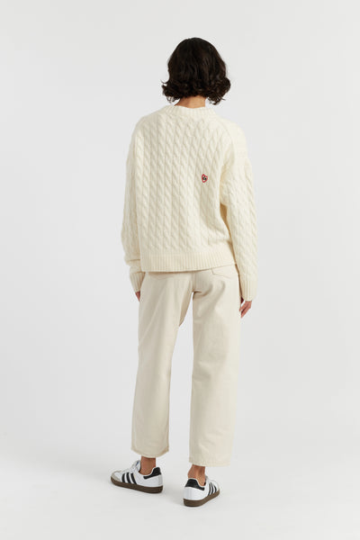 Person wearing a white textured sweater and cream pants on a white background