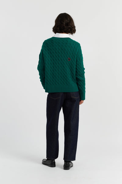 Person wearing a green textured sweater and dark pants on a white background