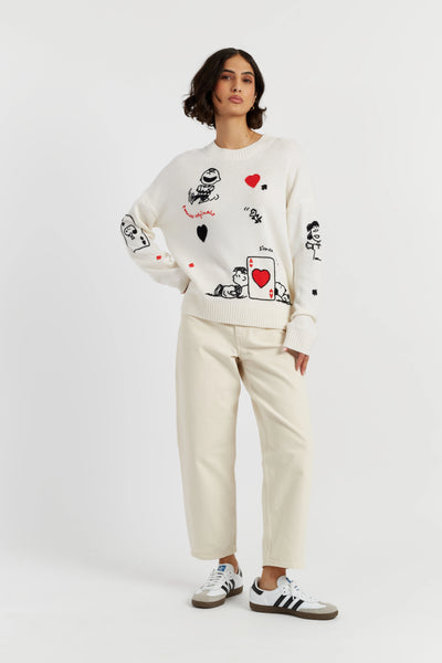 Person wearing a white sweater with graphic designs and beige pants on a white background