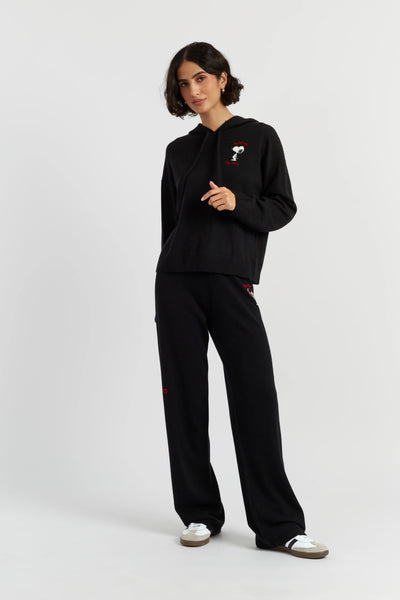 Person wearing a black outfit with a small red and white design on a plain background