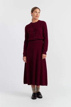 Woman wearing a burgundy outfit with a sweater and skirt on a white background