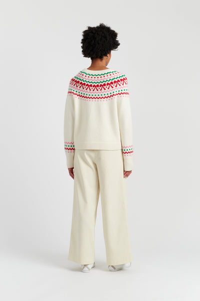 Person wearing a cream sweater with a colorful pattern on the back, standing against a white background