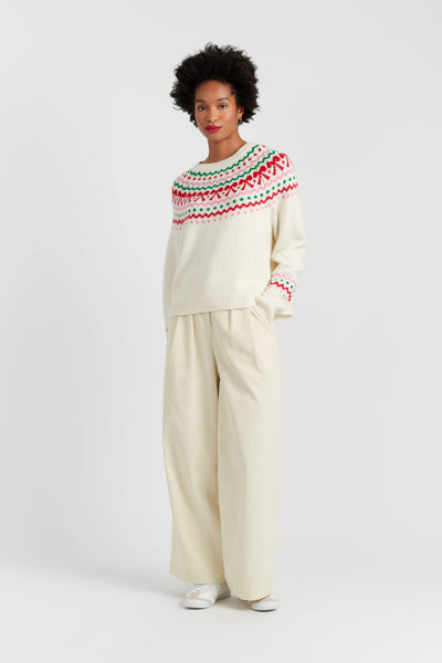 Person wearing a white sweater with red and green patterns and beige pants on a white background