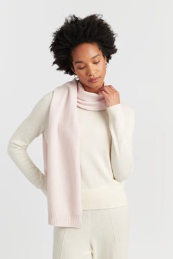 Woman wearing a light pink scarf and white sweater on a plain background