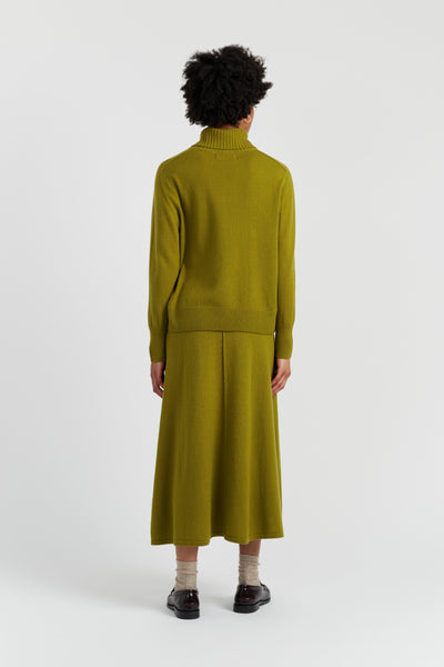 Person wearing a green sweater and skirt set on a white background