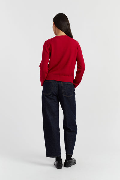 Person wearing a red sweater and dark jeans on a white background