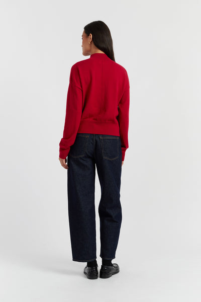 Person wearing a red sweater and dark jeans on a white background