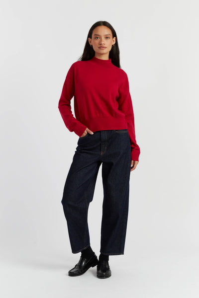 Person wearing a red sweater and dark jeans on a white background
