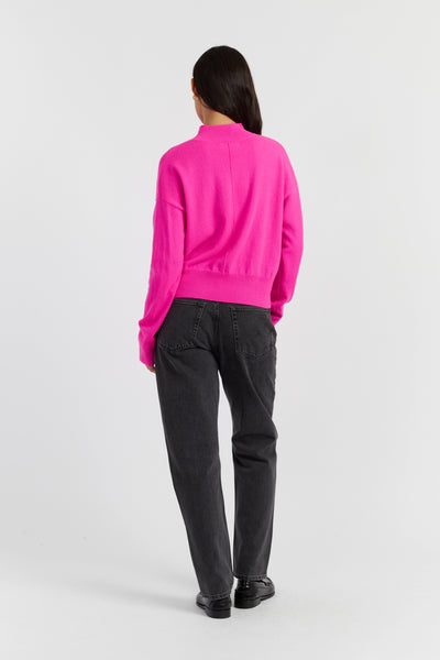 Person wearing a bright pink sweater and black pants on a white background