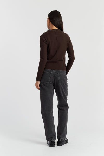 Person wearing a brown sweater and dark jeans on a white background