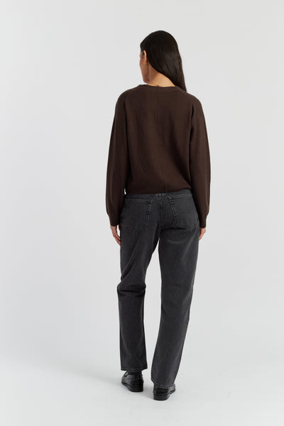 Person wearing a brown sweater and dark gray pants on a white background