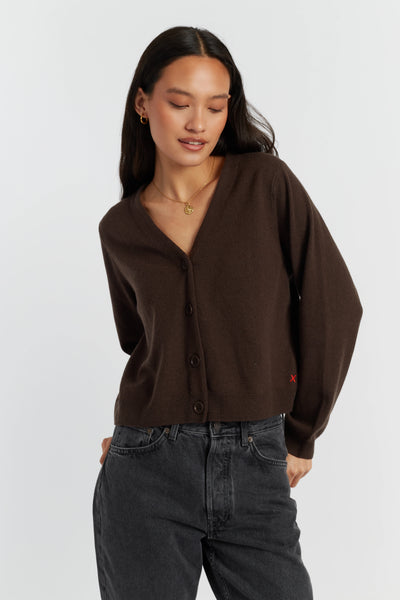 Woman wearing a brown cardigan and dark jeans on a white background