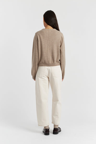 Person wearing a beige sweater and white pants on a white background