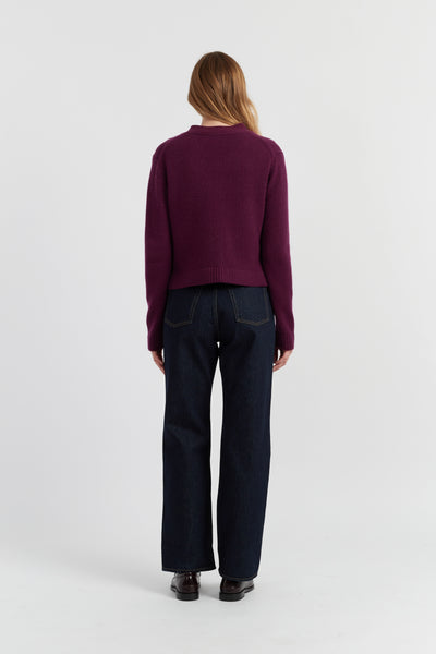 Person wearing a purple sweater and dark jeans on a white background