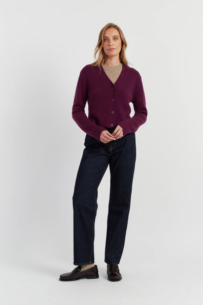 Woman wearing a purple cardigan, navy pants, and black shoes on a white background