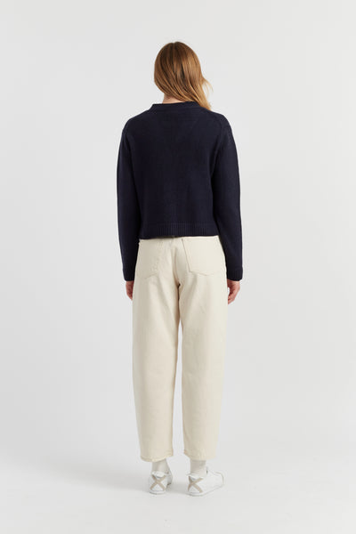 Person wearing a navy sweater and white pants on a light gray background