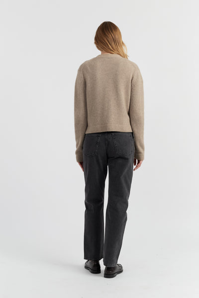 Person wearing a beige sweater and dark pants on a white background