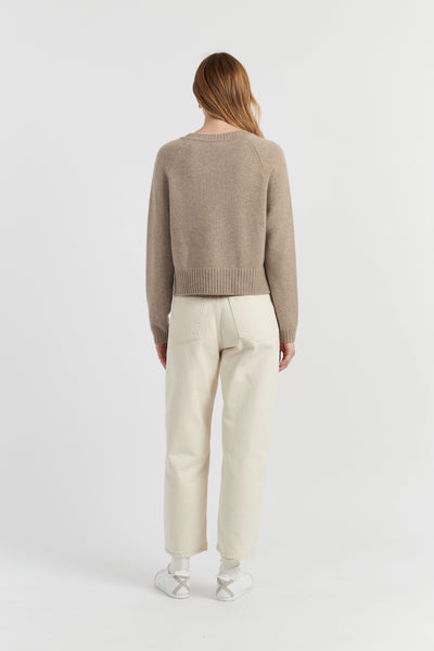 Person wearing a beige sweater and white pants on a white background