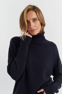 Woman wearing a navy blue turtleneck sweater against a white background