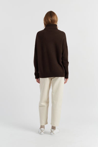 Person wearing a brown sweater and white pants on a white background