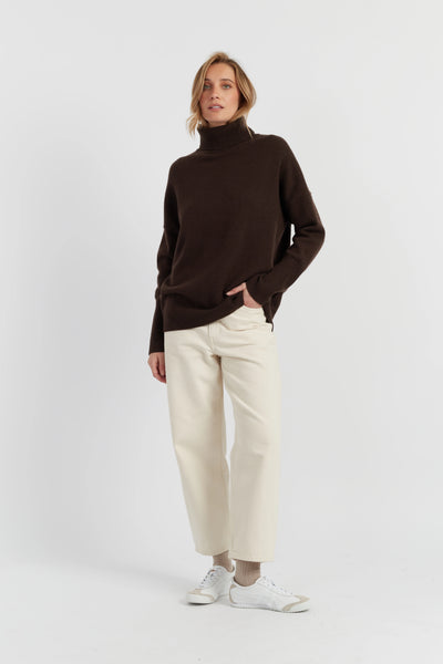 Woman wearing a brown turtleneck sweater and white pants on a white background