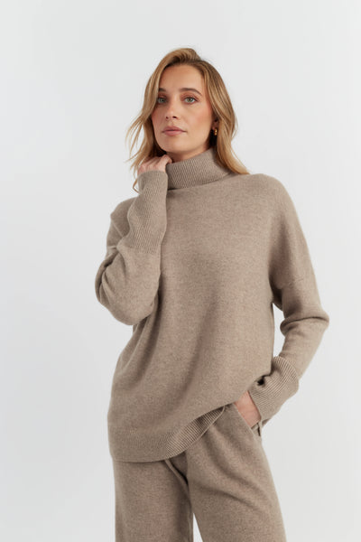 Woman wearing a beige turtleneck sweater and pants on a white background