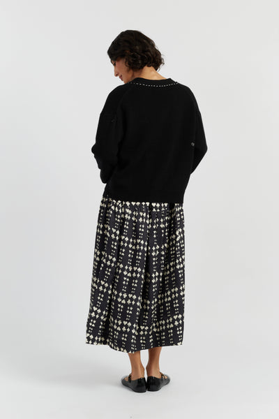 Person wearing a black sweater and patterned skirt on a white background