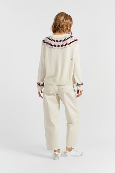 Person wearing a cream sweater with purple and red pattern and matching pants on a white background