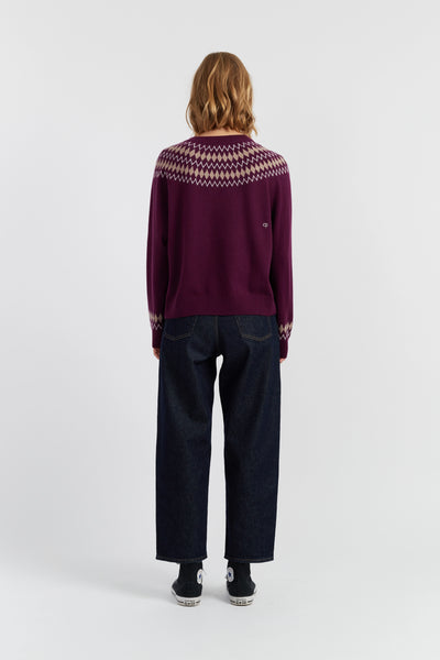 Person wearing a patterned purple sweater and dark jeans on a white background