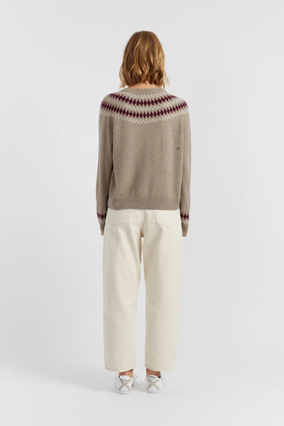 Person wearing a patterned sweater and white pants on a white background