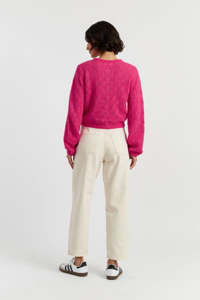 Person wearing a pink sweater and white pants on a white background