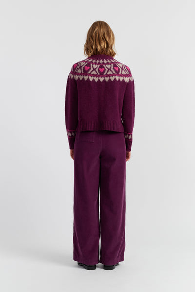 Person wearing a purple sweater with a patterned yoke and matching pants on a white background