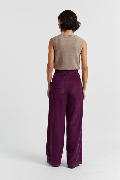 Person wearing a beige sleeveless top and purple pants on a white background
