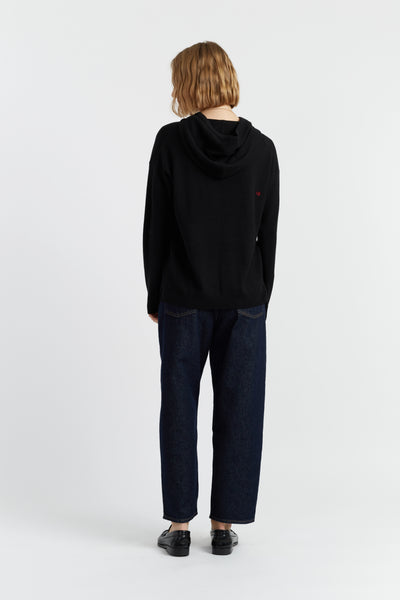 Person wearing a black hoodie and dark pants on a white background