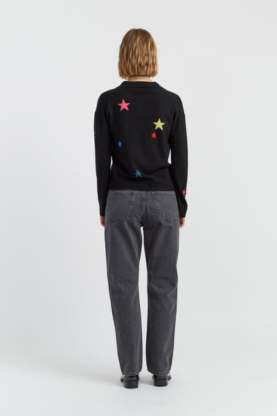 Person wearing a black sweater with colorful star patterns on the back, standing against a white background.