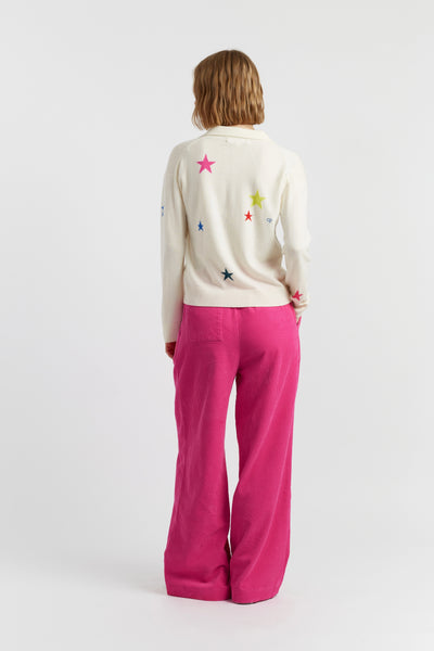 Person wearing a cream sweater with colorful star patterns and pink pants on a white background