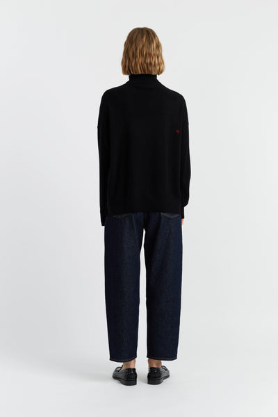 Person wearing a black sweater and dark pants on a white background